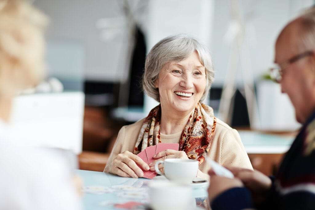 - The Preserve Cheerful senior woman laughing and playing cards with friends over coffee in a social gathering.
